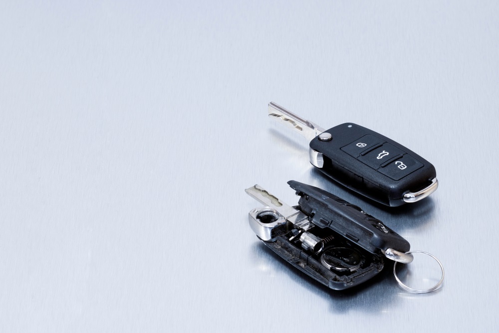 Locksmith broken or damaged car key fob and new remote vehicle key on aluminium background. Repair of broken or damaged remote key fob of any vehicle car service.